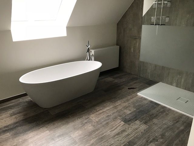 Badkamer onder een dakschuinte met vrijstaand bad, vloer in keramisch parket en een inloopdouche met glaswand