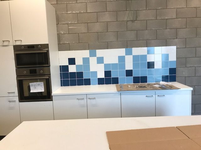 Witte keuken met een spatwand in blauw mozaiek naast de inbouwovens