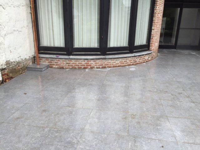 Terras in blauwe steen rond een ronde erker met donkere ramen