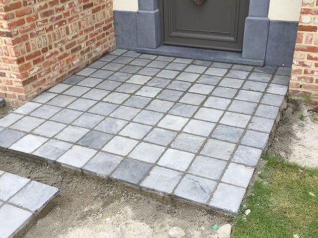Tuinzijde van het terras in blauwe steen, met de kantopsluiting tegen het gazon