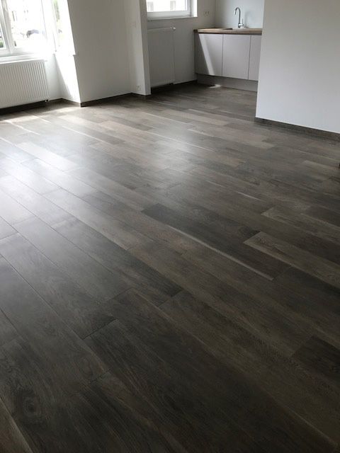 Donkere vloer met houtmotief tegen een witte plint